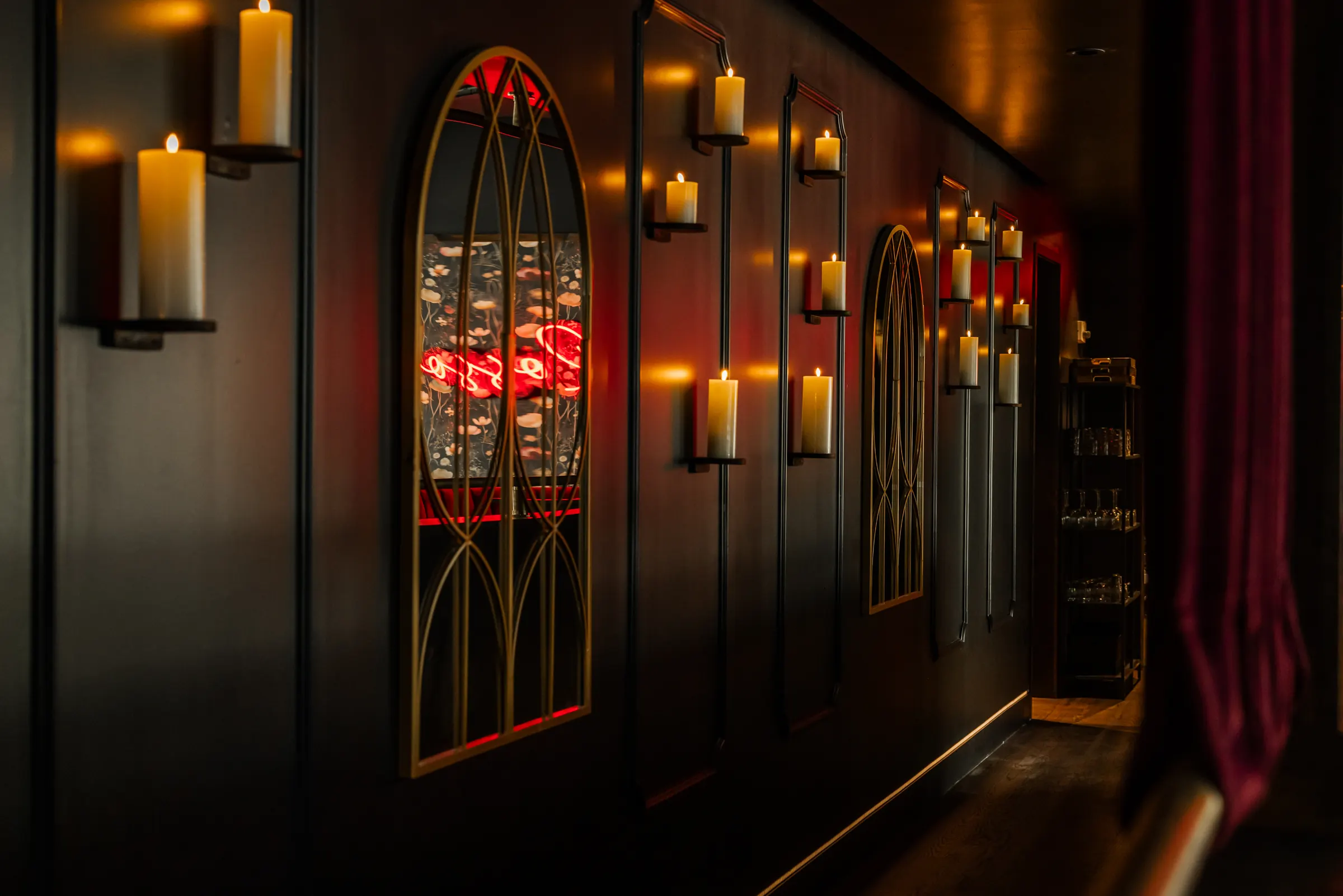 Candle sconces and arched mirrors along a dark hallway